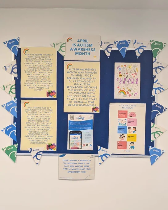 A picture of a noticeboard in the Marsden House, Chester, waiting room. On the noticeboard there is Autism Acceptance Month bunting, pictures of puzzle pieces and infinity symbols, and printed information about Autism Awareness Month.