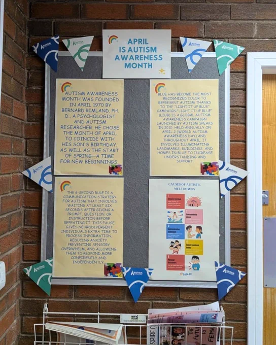 A picture of a noticeboard in the Mill Street, Crewe, waiting room. On the noticeboard there is Autism Acceptance Month bunting, pictures of puzzle pieces and infinity symbols, and printed information about Autism Awareness Month.