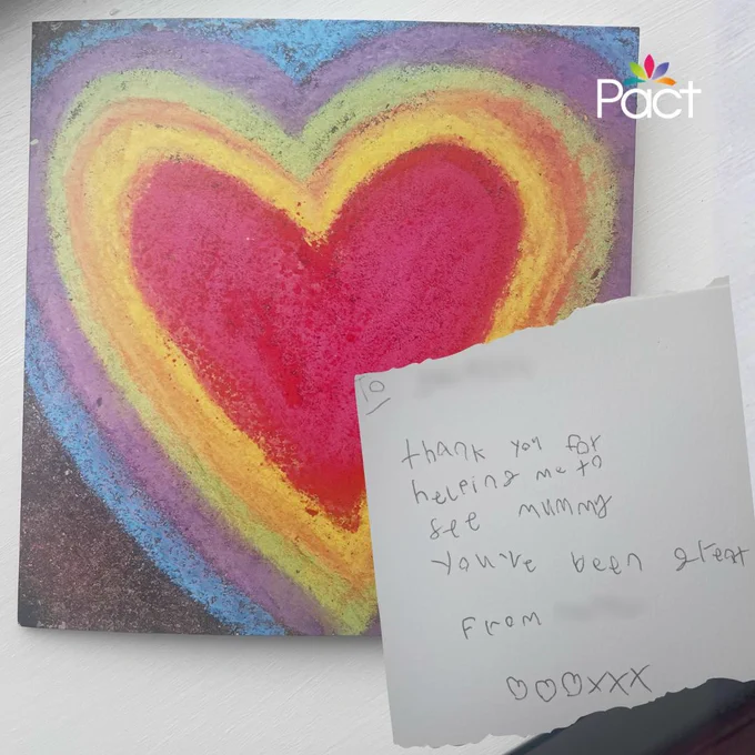 A child’s handmade thank you card on a light surface. The card shows a large rainbow‑coloured heart drawn in chalk or pastels. Over the corner is a handwritten note from a child saying thank you for helping them see their mum, with kisses drawn at the bottom. The Pact logo appears in the top right corner.