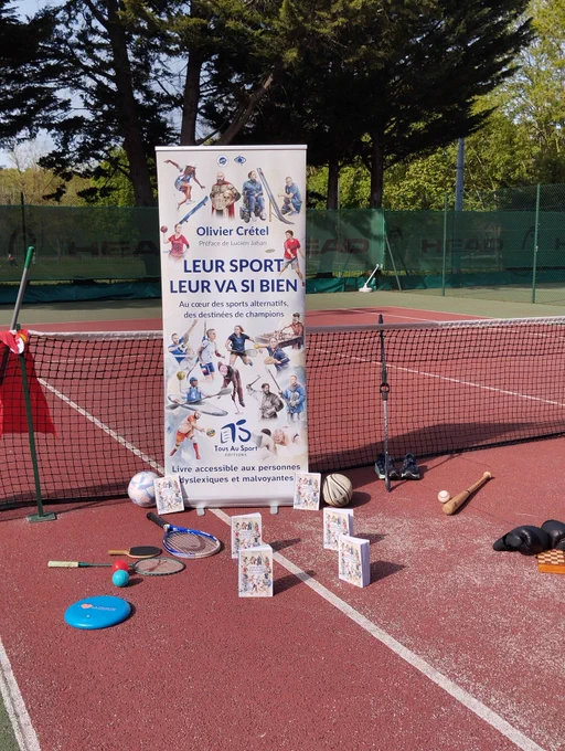 Un roll up reproduisant la couverture de Leur Sport Leur Va Si Bien est positionné sur un court de tennis avec 6 livres et des objets évoquant différents sports à l'honneur dans l'ouvrage.