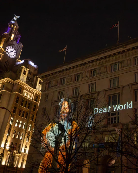 Projected film ‘Hand Ships Sail’ by Cathy Mager is lighting up the side of the Cunard building. A woman is using BSL and next to her are the words ‘Deaf World’. Credit Brian Roberts
