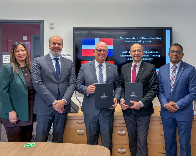 Five people in business attire posing for a photo. Two hold Carleton-branded folders.