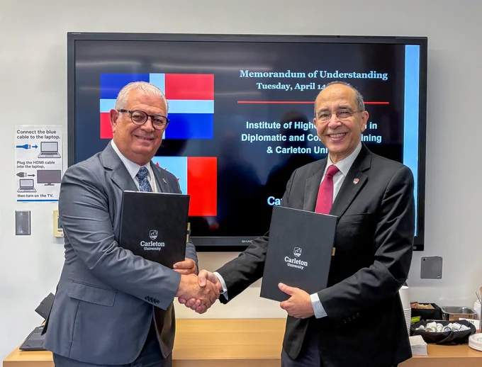 Two men in business attire shaking hands and holding Carleton-branded folders.