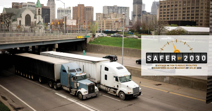 Image of two semi-trucks driving in an urban setting withe SAFERY by 2030 logo on the right.