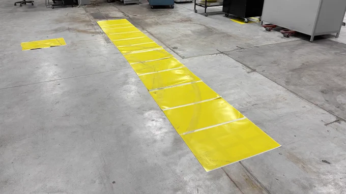 Long row of rectangular yellow floor panels marking space for equipment on a concrete warehouse floor