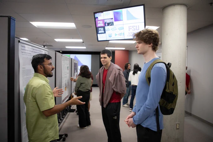 A student gesturing while presenting his research poster for two attendees at the 2026 Computational Exposition event.