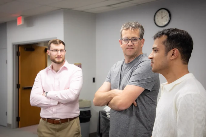 Two faculty members listen intently as a student presents his research poster.