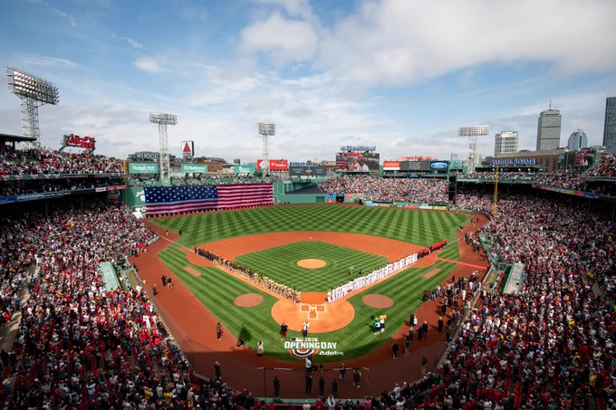 Wide shot of Fenway Park with the American flag draped over the Green Monster. The entire Red Sox roster and Padres roster are lined up down each base line. An on-field stencil reads "Opening Day 2026."