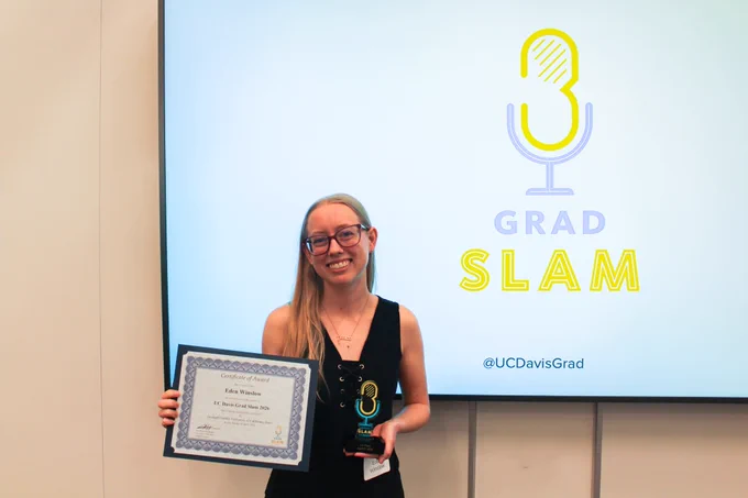 Eden Winslow smiling in front of the UC Davis Grad Slam backdrop and holding the first place trophy and certificate.