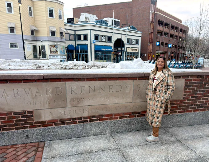 Komal Dhoot in front of a brick wall that says Harvard Kennedy School