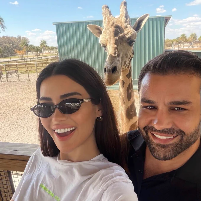 A woman and a man taking a selfie in front of a reticulated giraffe at the top of the giraffe platform at Wild Florida's Drive-thru Safari Park.