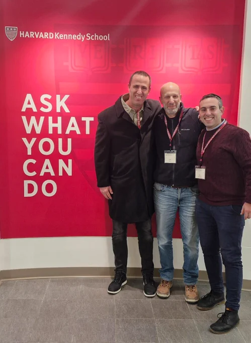 Three executive education participants in front of the Harvard Kennedy School "Ask What You Can Do" banner