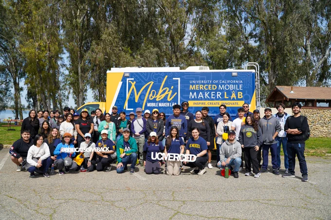 A diverse group of students and alumni pose together after a lake cleanup.