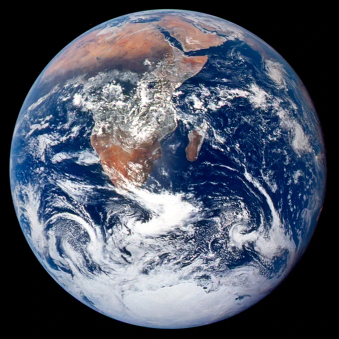 Photograph of Earth captured by the Apollo 17 crew on December 7, 1972. Earth takes up most of the image. Dark blue ocean water and swirling white clouds are visible. Africa is a large brown landmass from the center to the upper left, stretching from about 9 to 12 o'clock. Clouds cover most of the 6 o'clock. Credit: NASA