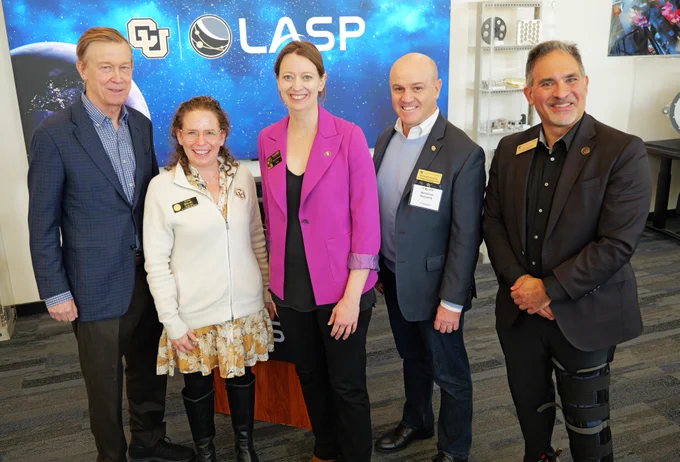 Senator John Hickenlooper, left, is joined by Regent IIana Speigel, LASP Director Bethany Ehlmann, Senior Vice Chancellor for Research and Innovation and Dean of Institutes Massimo Ruzzene and Chancellor Justin Schwartz during a visit to LASP at the University of Colorado Boulder. They're in a room with various scientific displays. They're standing in front of a backdrop with CU and LASP logos.