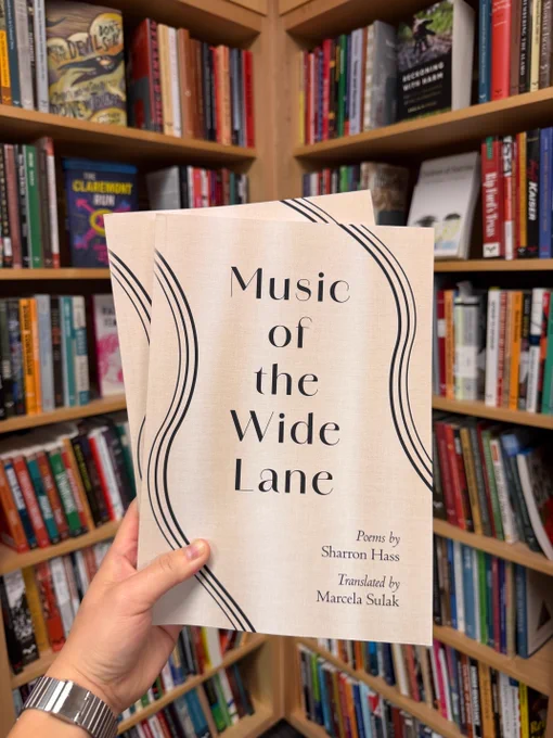 Two books of the Music of the Wide Lane, it is a cream colored book with light design on the left side. The books are being held in front a bookshelf full of books.