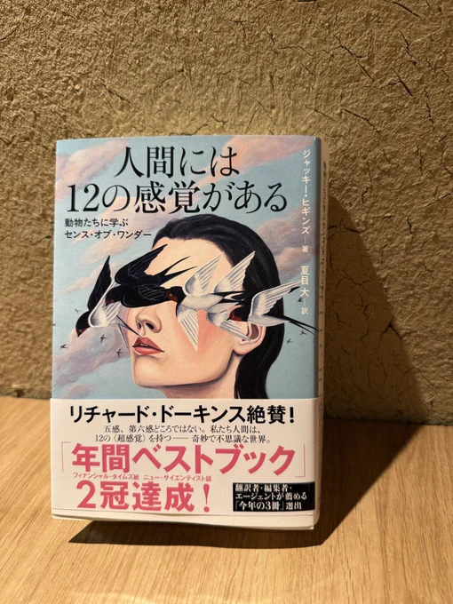 書籍『人間には12の感覚がある』。ひび割れた土壁を背景に、女性の顔の前をツバメの群れが横切る幻想的なイラストの表紙。帯には年間ベストブック受賞の文言が記されている。