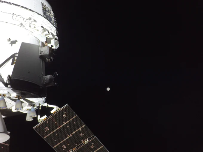 The gray Moon can be seen in the vast distance against the blackness of space. A partial view of the white Orion spacecraft can be glimpsed on the left side of the image. One of its paneled solar array extends into the center bottom of the image. Credit: NASA