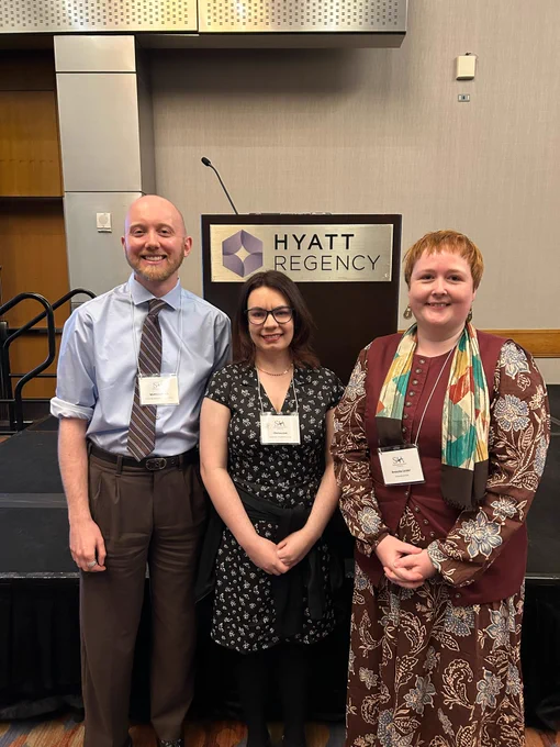 Image of three early career academics standing in front of a podium. End ID.