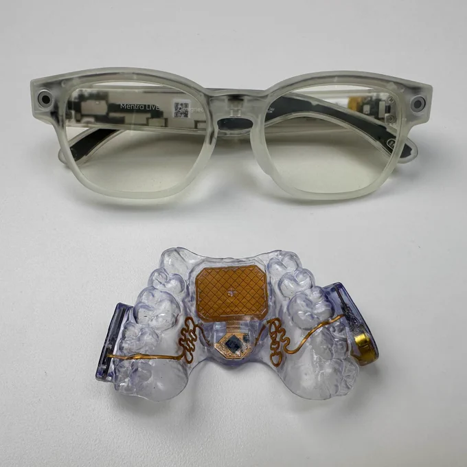 Transparent Mentra glasses above the Augmental MouthPad^ on a white surface. Both are wearable devices with clear housings that reveal their internal electronics.