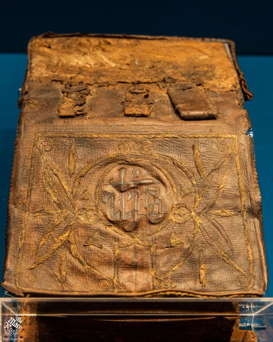 The leather pouch, showing the IHS monogram, a decorative pattern around it and the loops on the back that allowed it to be attached to a belt.