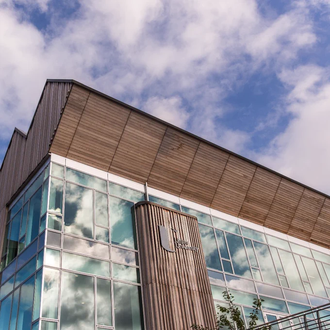 Modern Ulster University Coleraine campus building with large reflective glass windows under a partly cloudy blue sky.