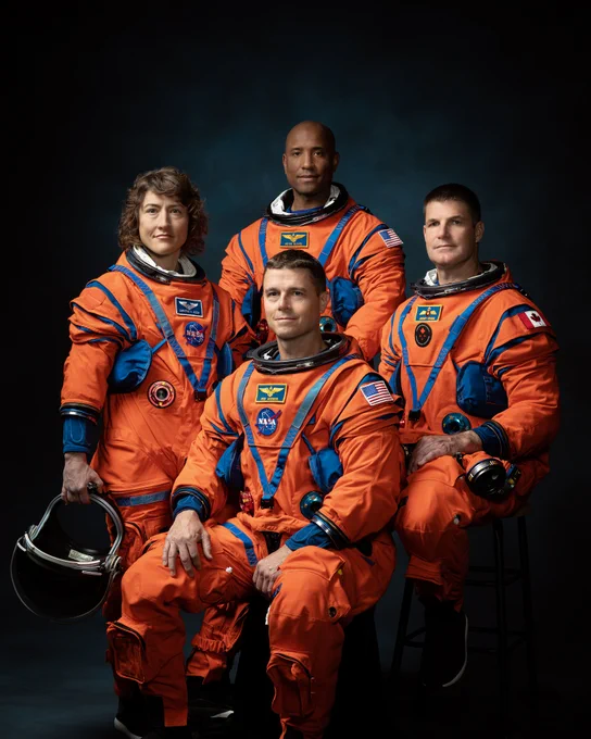 The Artemis II crew sits for their portrait in front of a dark background. Wearing orange suits with patches noting their names, nationalities, and NASA or CSA. From left to right, are Christina Koch, Victor Glover, Reid Wiseman, and Jeremy Hansen. Koch holds a helmet in her hand. \u2063Credit: NASA/Josh Valcarcel\u2063