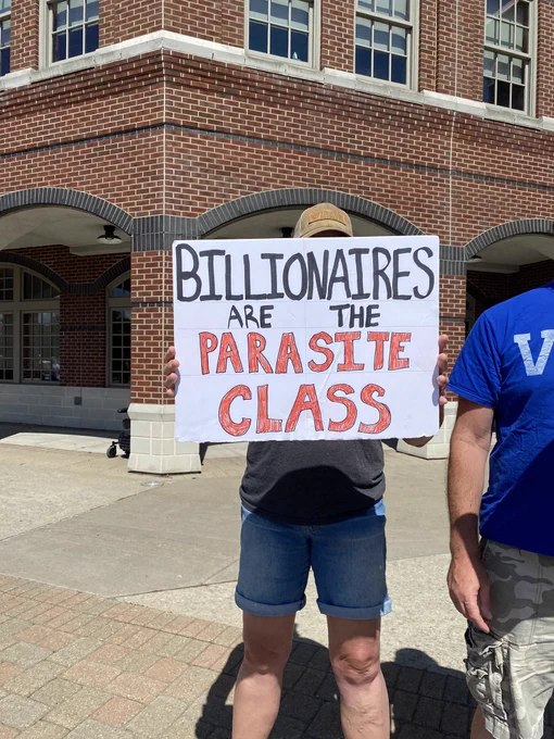 Comrade holding up a sign that says “billionaires are the parasite class”