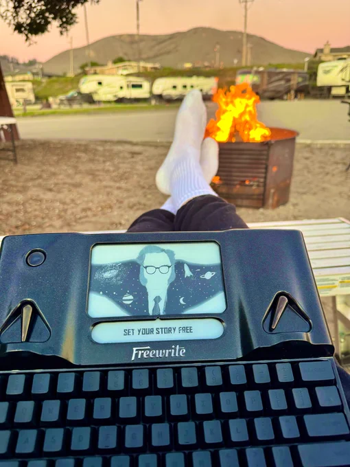Person writing on a Freewrite by a fire at dusk.