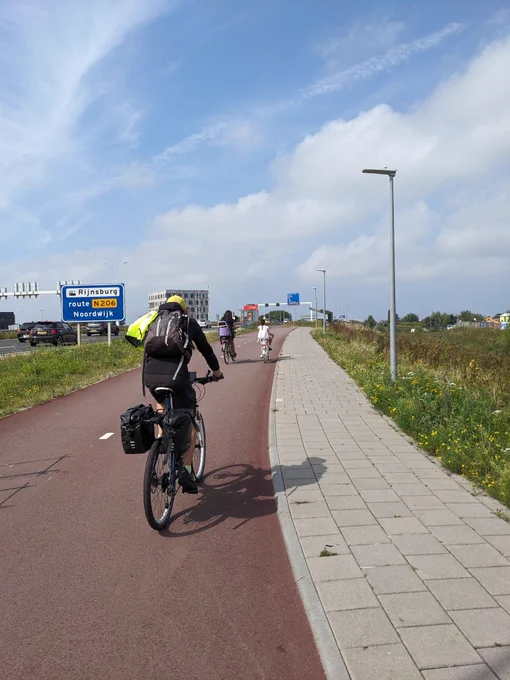 Ein Fahrradfahrer samt Rucksack und Gepäckträgertaschen auf einem rot asphaltierten Zweirichtungsradweg in Den Haag,  der gerade neben einer Autobahn verläuft 
