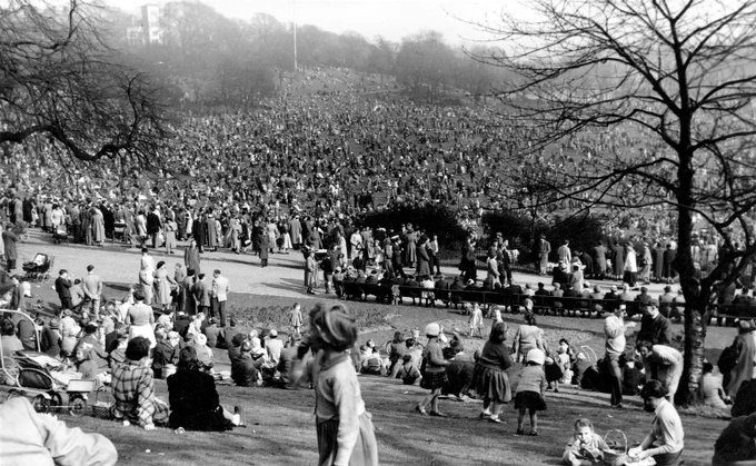 Large crowd gathered on a hillside park during a public event on a foggy day.