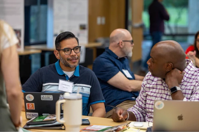 Two participants at UNT's 2025 project-based learning symposium sit at a table and talk.