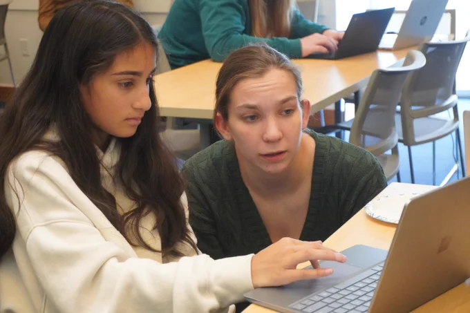 An MIT student guides a middle school student on a laptop.