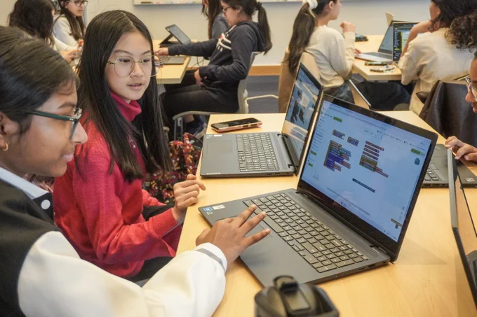 Two students working on MIT App Inventor projects on their laptops.
