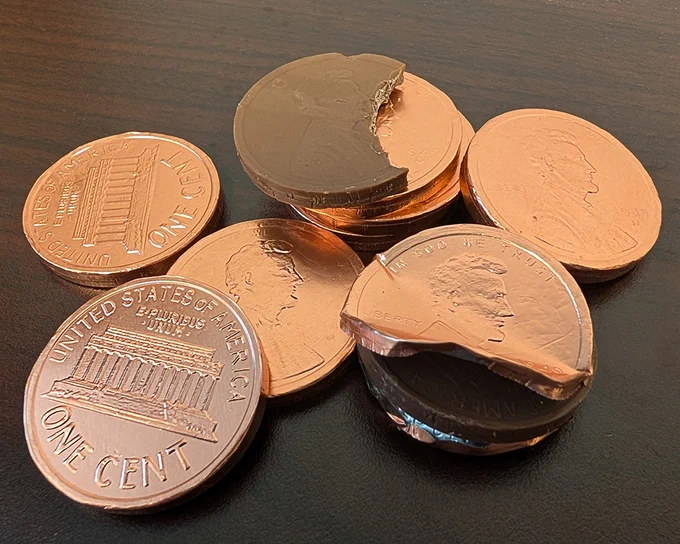 Stack of U.S. pennies on a dark surface, with two coins partially bitten to reveal chocolate inside.