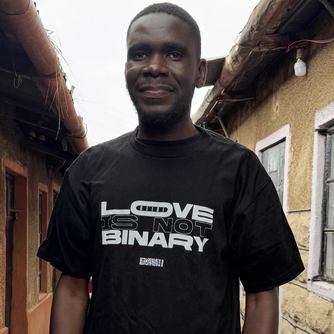 Black T-shirt featuring "LOVE IS NOT BINARY" text with binary code and barcode design by hirano taichi. A statement piece questioning binary views on gender and love.