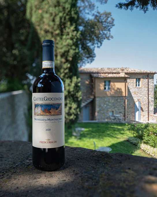 A bottle of Marchesi Frescobaldi wine placed on grassy ground in front of a stone building surrounded by trees at Tenuta CastelGiocondo.
