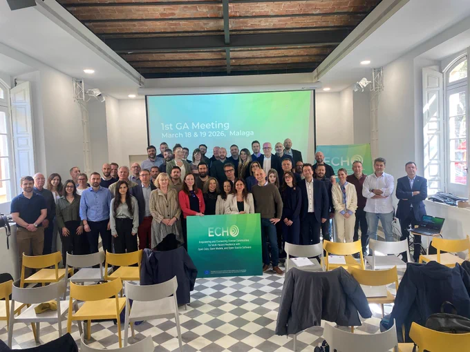Image shows the ECHO consortium standing in front of a projector with two ECHO-branded banners. The projector says '1st GA Meeting, March 18 & 19 2026, Malaga'. Chairs are in front of the consortium.