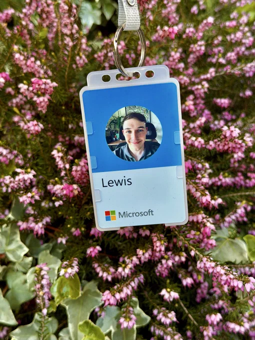 Microsoft blue employee badge with a photo of Lewis, the name “Lewis’ and lots of small pink flowers in the background.