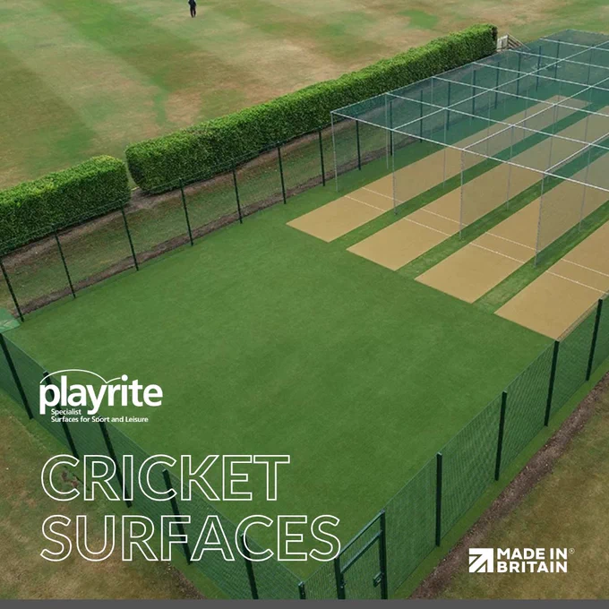 A cricket practice net area with artificial turf and pitch strips enclosed by fencing and surrounded by trimmed hedges.