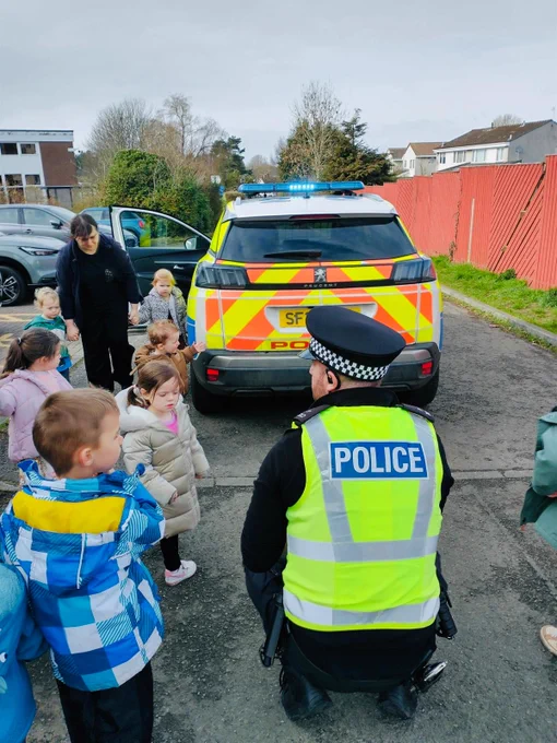 A police officer speaking to children outside with a marked police car