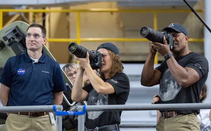 Two astronauts practice using cameras to take photographs while an instructor guides them 