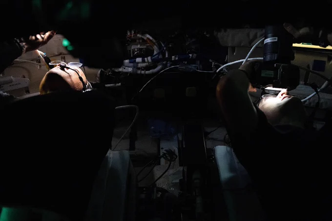 Two astronauts on the Artemis mission looking out windows on their spaceship. One is using a camera to take pictures 