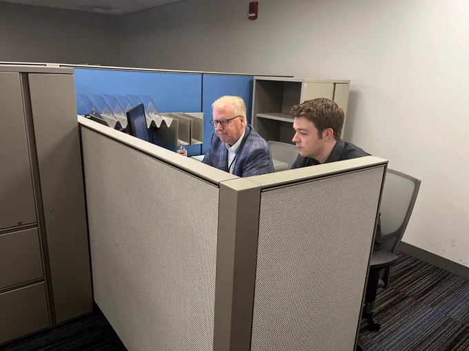 DRS Commissioner Mark Boughton sits in a cubicle and takes taxpayer phone calls with a fellow DRS employee. 