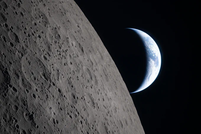 Earth setting behind the Moon as seen by the Artemis II crew. Over half the left side of the image is filled by the gray lunar surface, pocked with craters. Credit: NASA