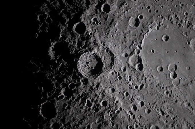 A close view of the Moon. Jagged circles of craters dot the gray surface, fading to dark on the left side of the image. Credit: NASA