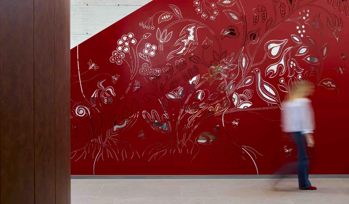 Abstract floral and leaf patterns in white and silver decorate a deep red wall in a modern interior space.