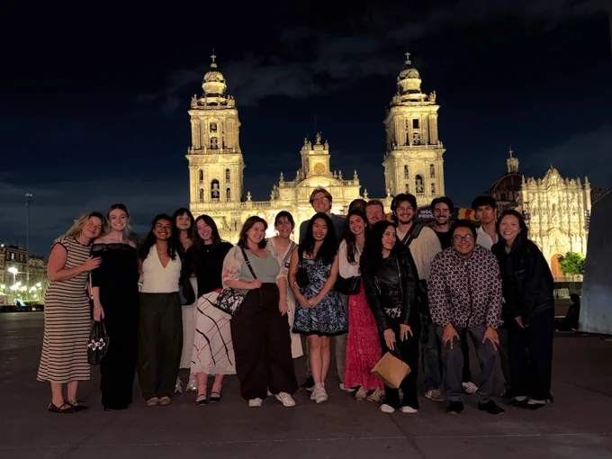 A group of people posing at night in front of the illuminated Mexico City Metropolitan Cathedral.