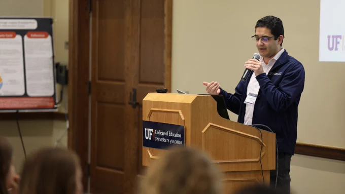 A person speaking in front of a crowd at a podium with the UF College of Education logo.