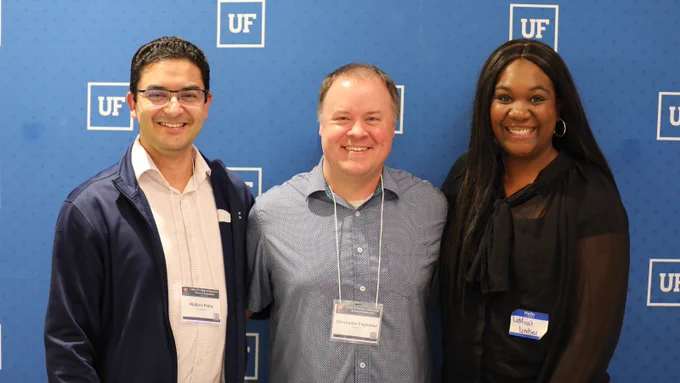 Three people standing in front of a blue background with the University of Florida logo pattern in white.